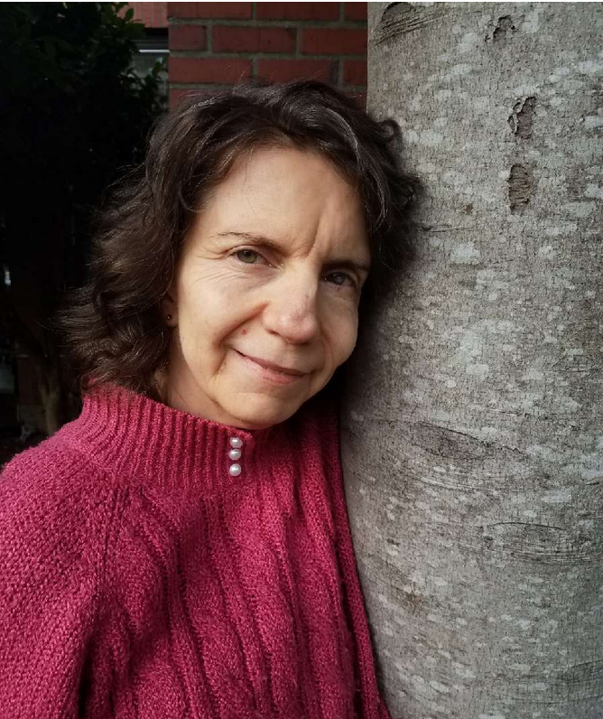 Photo of Callie next to a tree | Courageous Shifts™ Woman leaning against a tree with a warm smile, wearing a pink knit sweater outside.